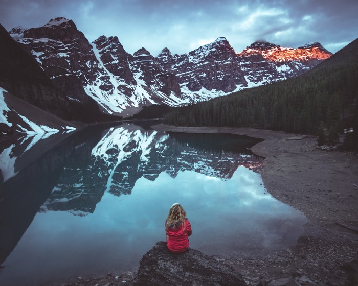 Woman sitting by Moraine Lake with snow-capped mountains