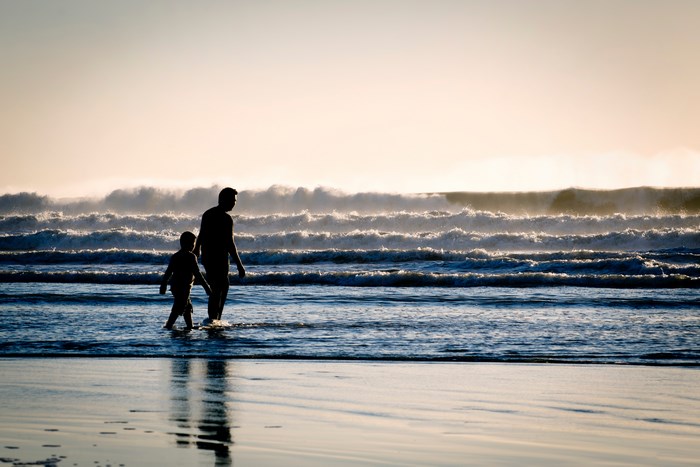 Father and son walking on the beach at sunset