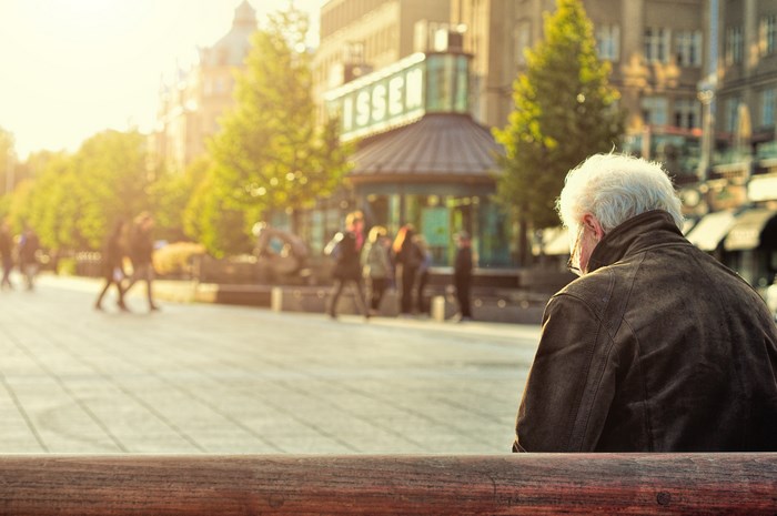 Elderly man sitting on a bench in a town square