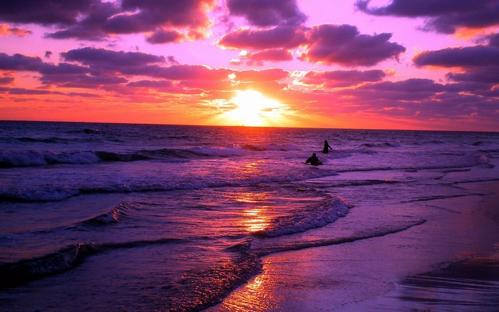 Purple and orange sunset over the ocean with waves and clouds