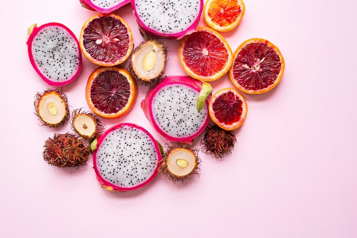 Dragon fruit, blood oranges, and rambutan slices on pink background