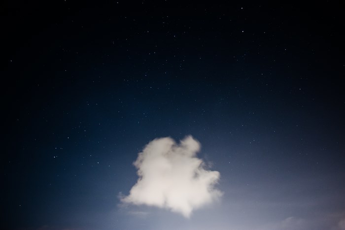 A single cloud floats in the night sky with stars