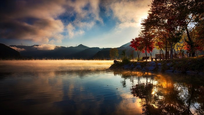 Misty lake at sunrise with autumn trees and mountains