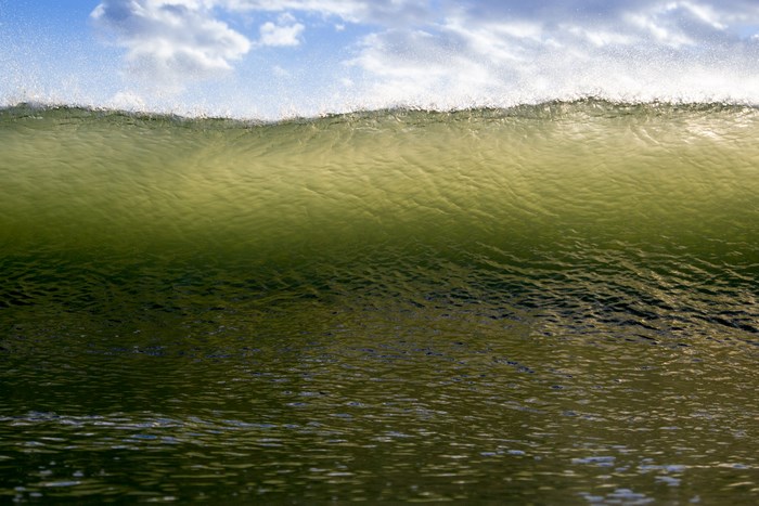 Green ocean wave with clouds in the sky