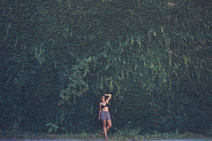 Woman in shorts and bikini top against a vine wall