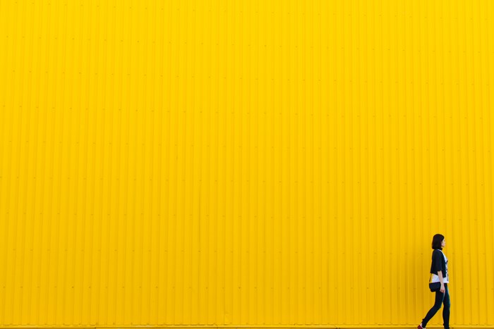 Woman walking in front of a yellow corrugated wall