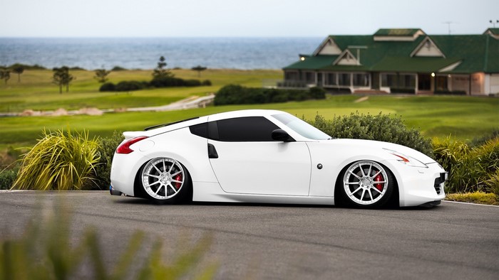 White Nissan 370Z on a road with a golf course and ocean in background