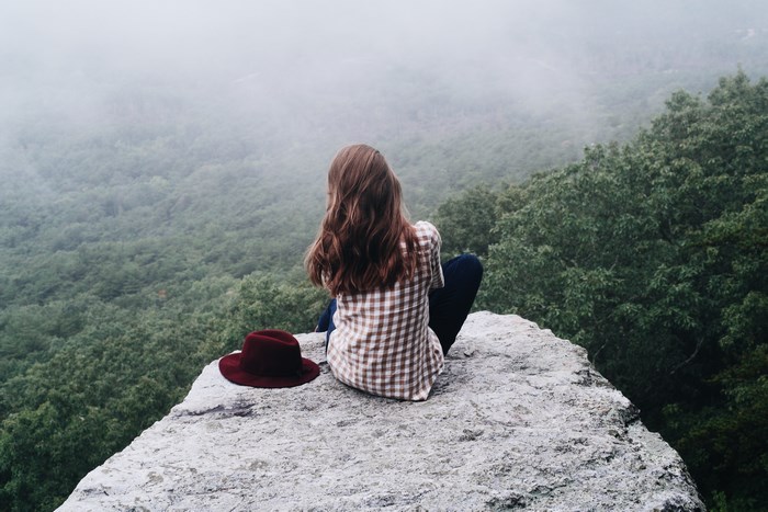 Woman sitting on a rock overlooking a foggy forest
