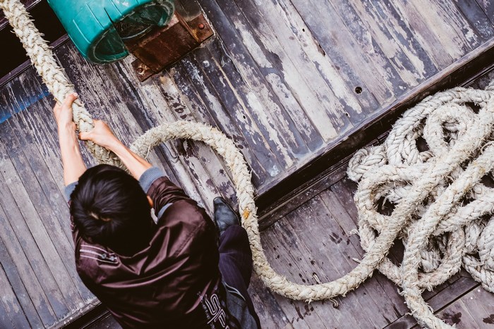 Man pulling a thick rope on a wooden deck