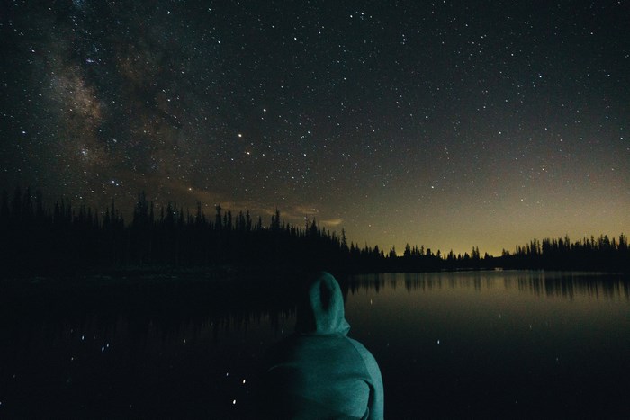 Person in hoodie looking at the Milky Way over a lake