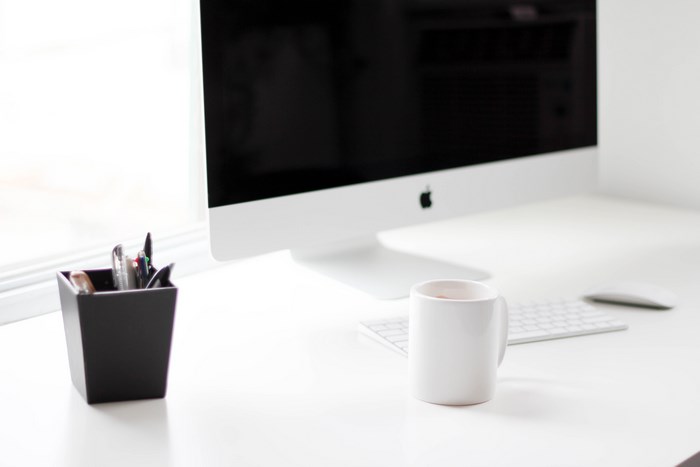 Apple iMac computer on a white desk with a mug