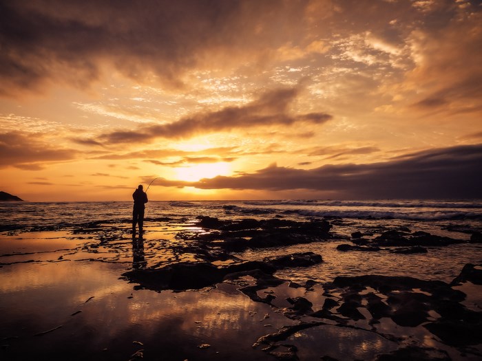 Fisherman silhouetted against an orange sunset over the ocean