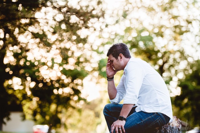 Man sitting outside with hand on forehead