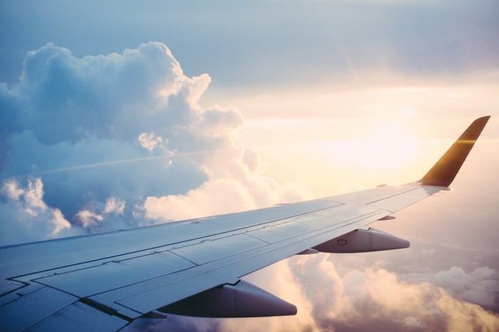 Airplane wing flying through clouds at sunset