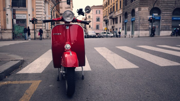 Red Vespa scooter on a crosswalk in Rome