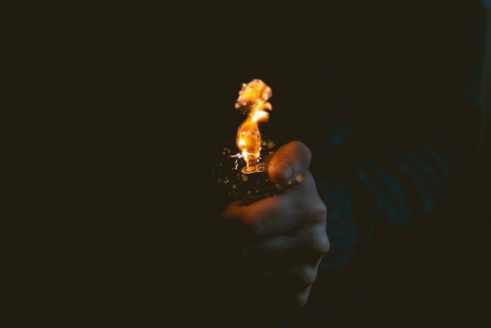 Hand holding a lit lighter with flames