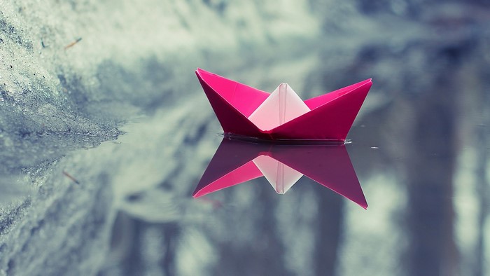 Pink paper boat floating on water with reflection