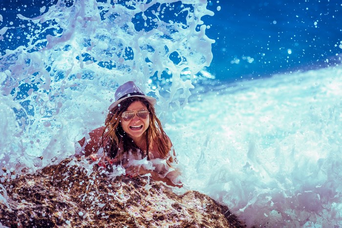 Woman in a hat and sunglasses splashes in ocean waves