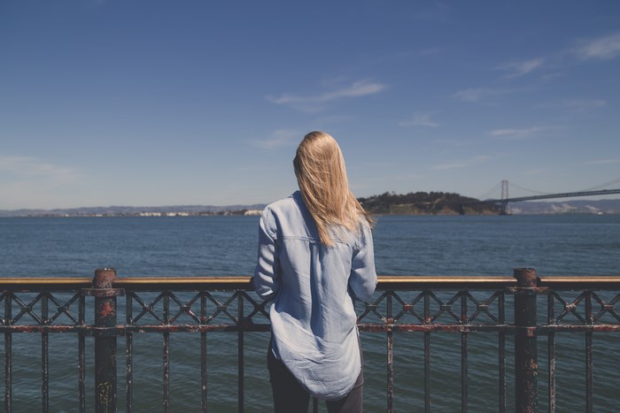 Woman in denim shirt looking at suspension bridge over water