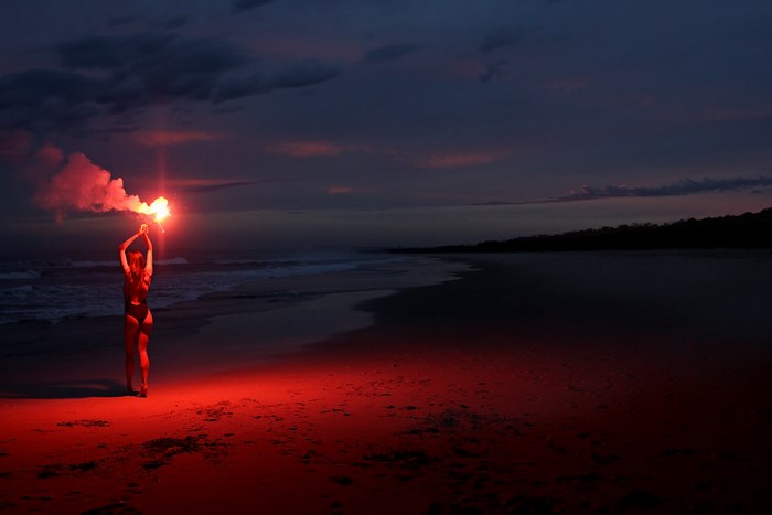 Woman holding a flare on a beach at dusk
