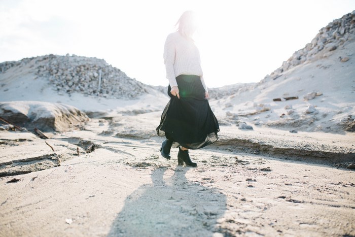 Woman in black skirt and white sweater walking in desert