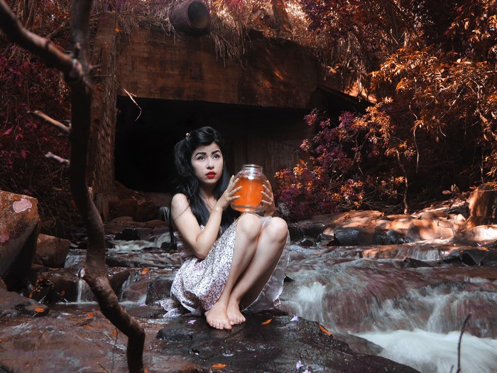 Woman Sitting by Creek Holding Jar of Honey