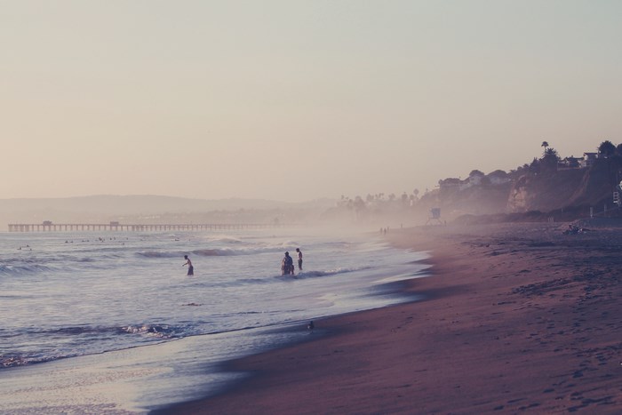 People swimming at the beach near a pier at sunset