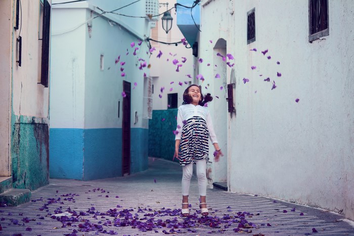 Girl throwing purple petals in Assilah alley