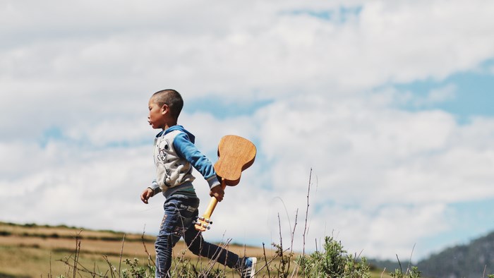 Boy running with a ukulele in a field