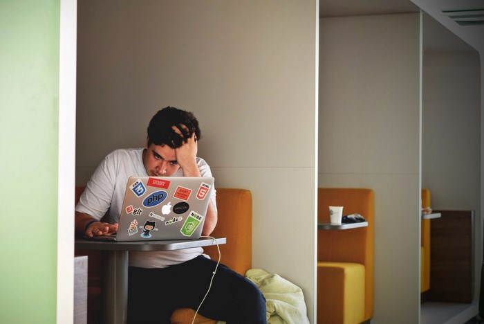 Man working on a sticker-covered Apple MacBook in a workspace booth