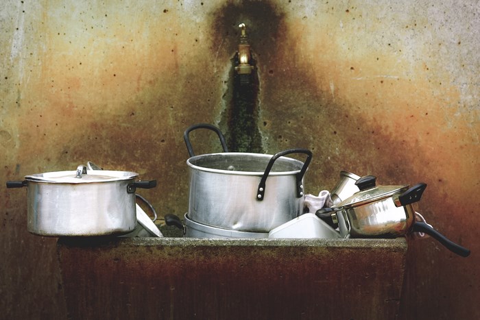 Aluminum pots and pans in a rustic sink with a faucet