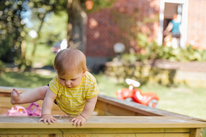 Baby climbing out of a sandbox in a garden