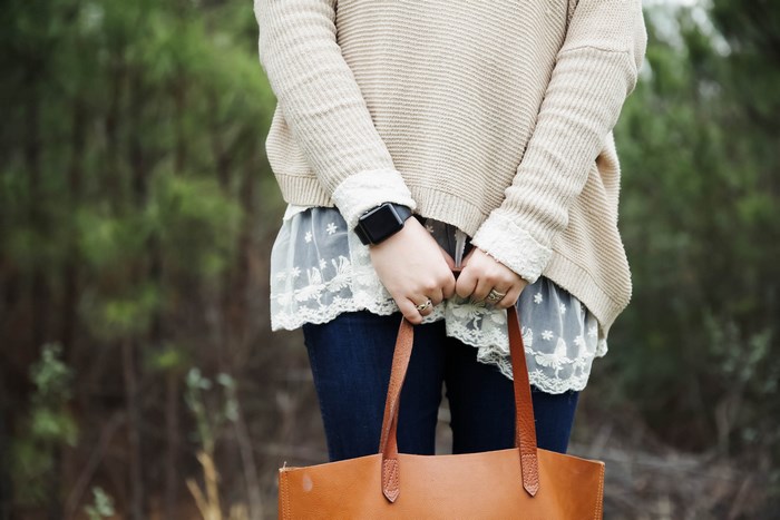 Woman wearing a sweater and lace trim holding a tote bag