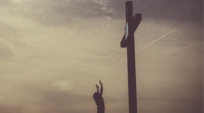 Silhouette of a person reaching towards a cross