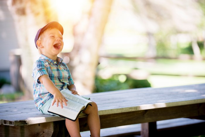 Boy in plaid shirt laughing with a book