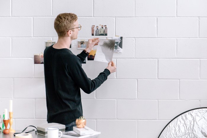 Man hanging photos on a white brick wall