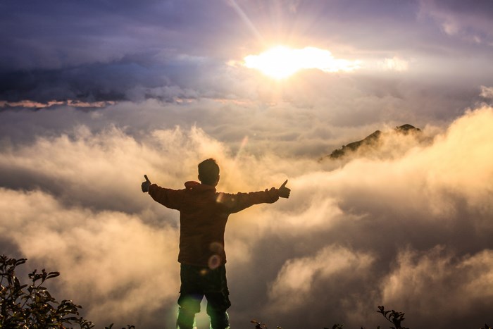 Man with arms outstretched on a cloudy mountain peak at sunrise