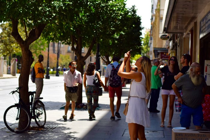 People walking on a sunny city street with trees and a bicycle