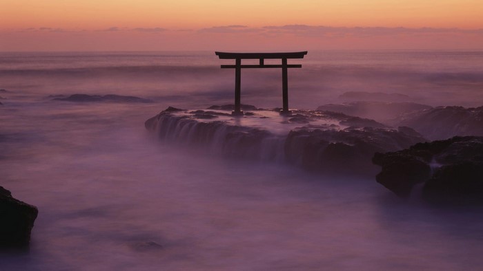 Torii gate on rocks in the sea at sunset