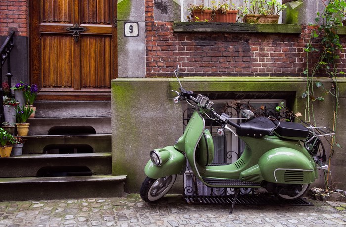 Green Vespa scooter parked by a brick building with a wooden door