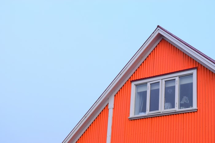 Orange house with pitched roof and window under blue sky