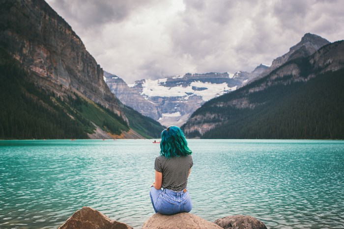 Woman with blue hair sitting by a turquoise lake in Canada