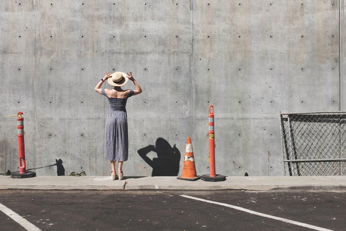 Woman in a dress and sun hat by a concrete wall