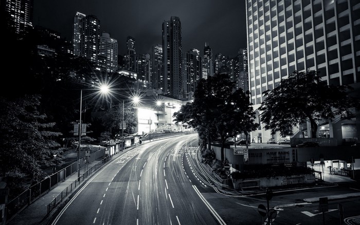 Monochrome urban cityscape at night with light trails on a highway