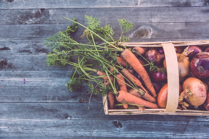 Basket of Carrots and Onions on Wooden Table