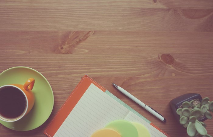 Coffee cup, notebook, pen, and plant on wooden desk