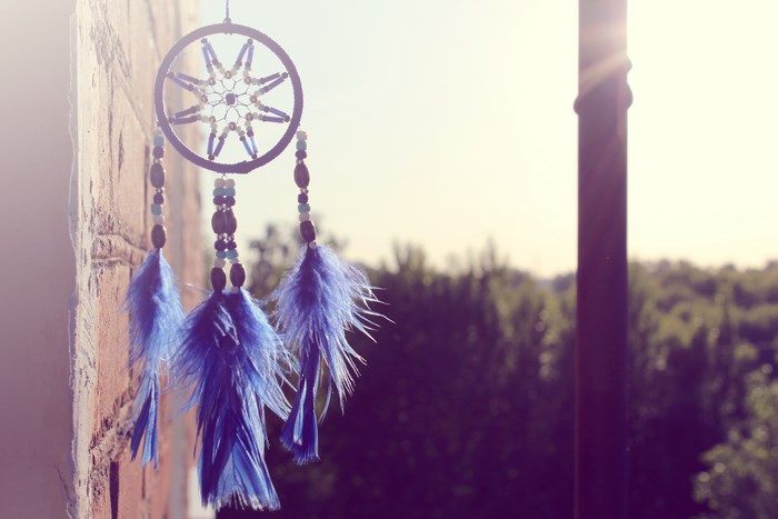 Dream catcher with blue feathers hanging on a brick wall