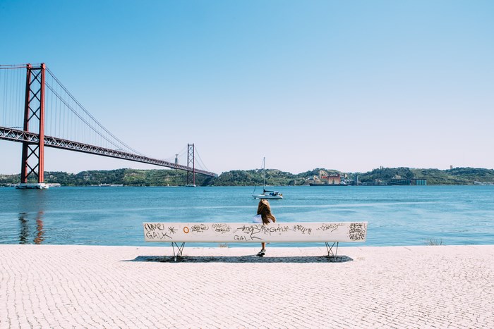 Woman sitting on a graffiti bench by the Tagus River with 25 de Abril Bridge