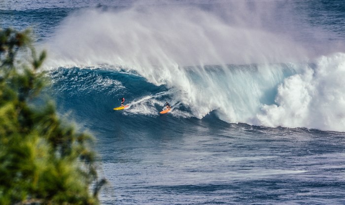 Two surfers ride a massive ocean wave