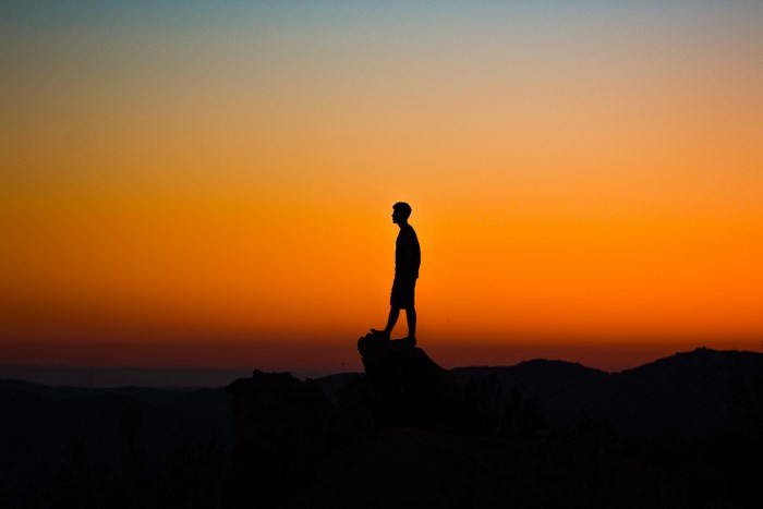 Silhouette of Man Standing on Rock at Sunset